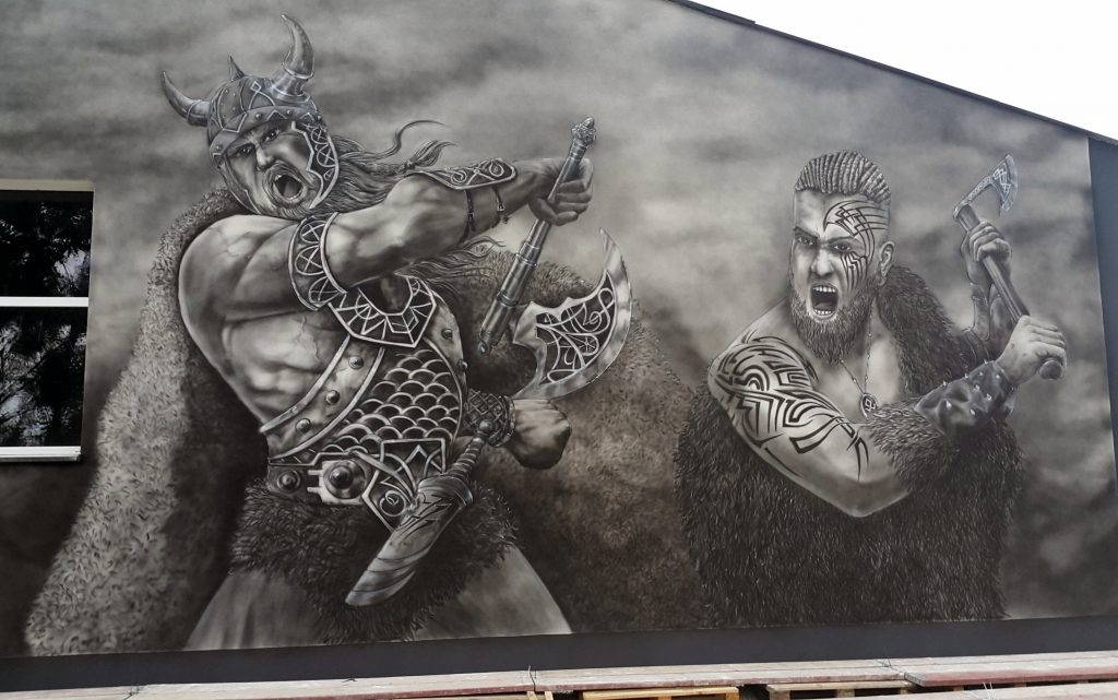 Czarno biały mural na elewacji budynku, wikingowie w boju